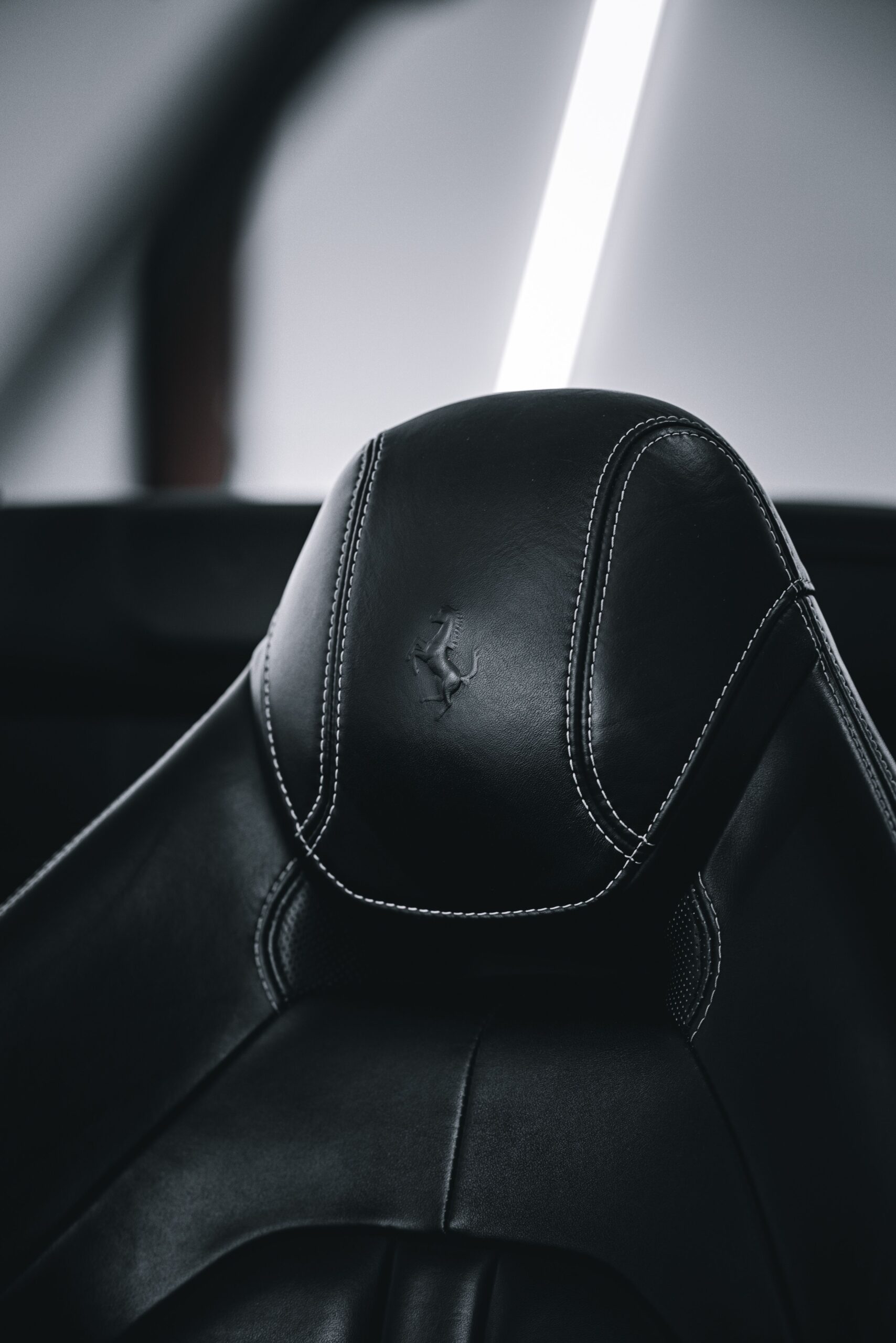 Close-up of a modern black leather car seat headrest with white stitching, offering a sense of luxury and comfort.