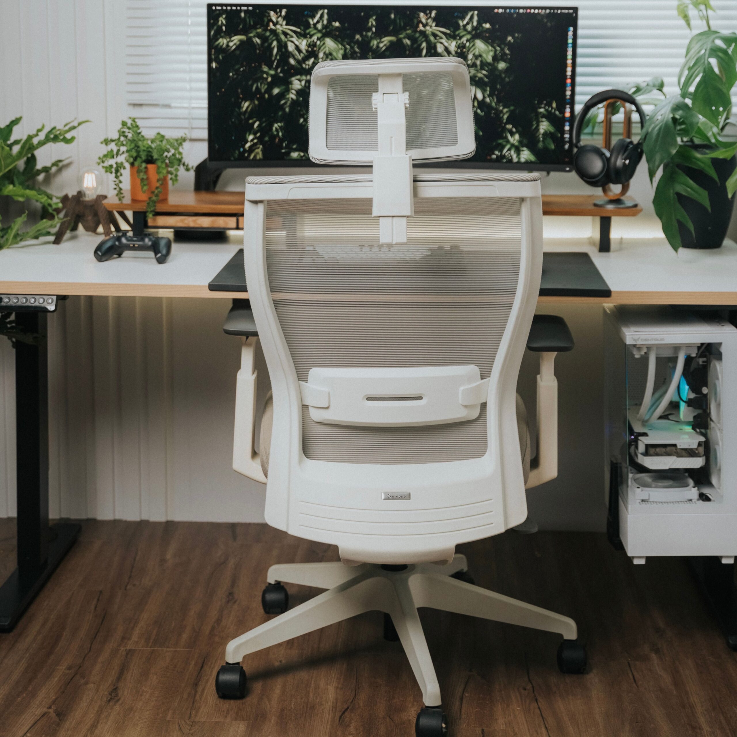 A contemporary office setup featuring a white ergonomic chair, large monitor, and potted plants.