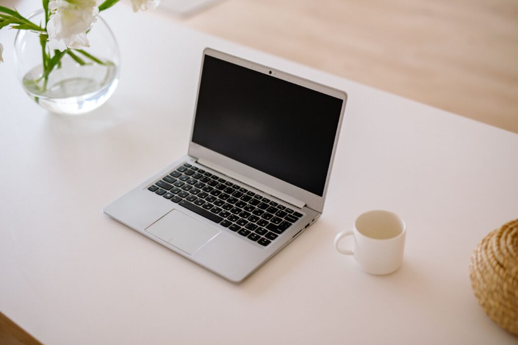 Why Using a Laptop Directly Destroys Your Neck A minimalist workspace with an open laptop, coffee mug, and vase on a bright indoor table.
