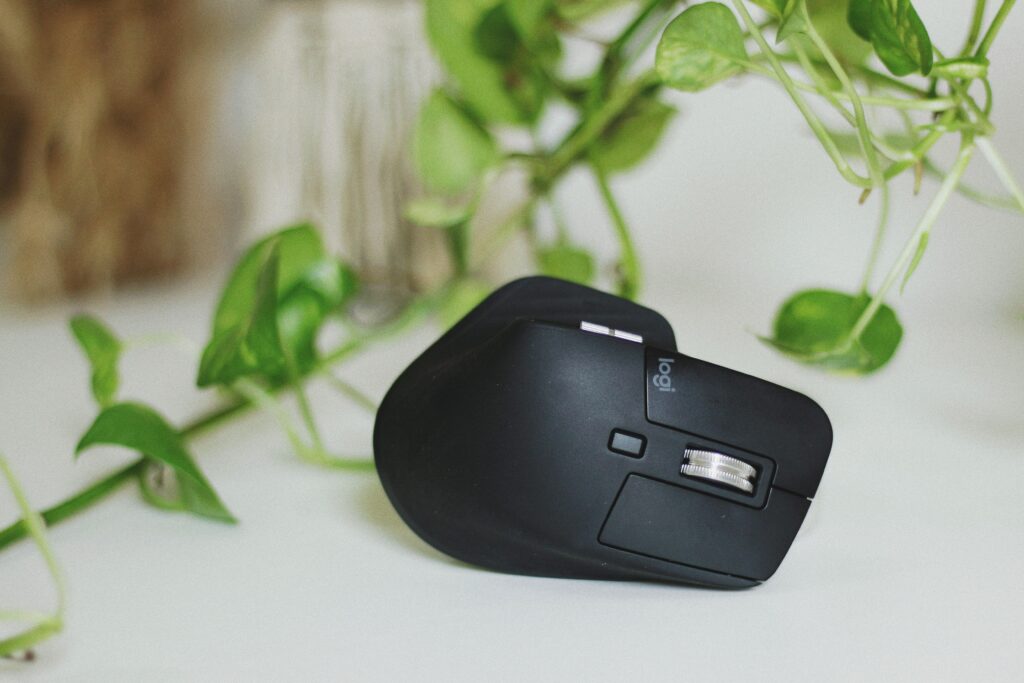 Black wireless mouse on a desk, surrounded by leafy green plants for a natural workspace vibe.