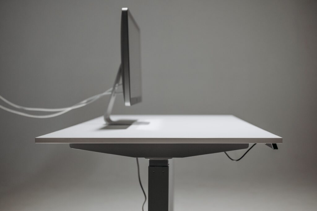 The Truth About Standing Desks: Why Standing Fails Side profile of a modern office desk with a computer monitor, emphasizing minimalism and technology.