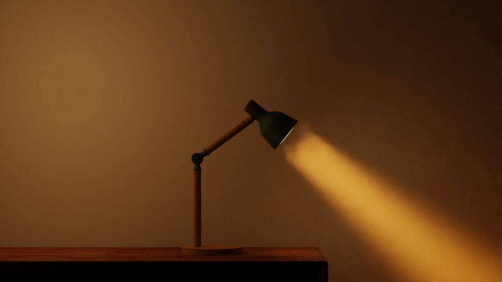 Where to Place a Desk Lamp to Stop Screen Glare A minimalist desk lamp casting a warm beam of light on a wooden surface.